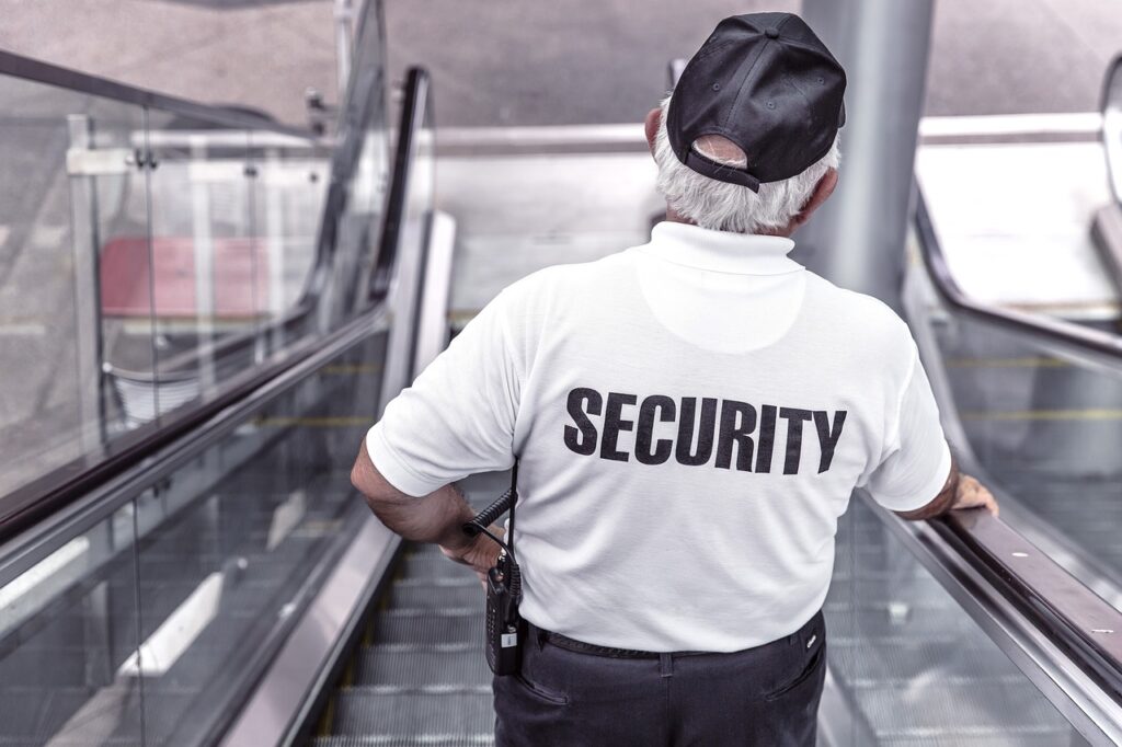 An elderly security guard observing surroundings while going down using escalator.